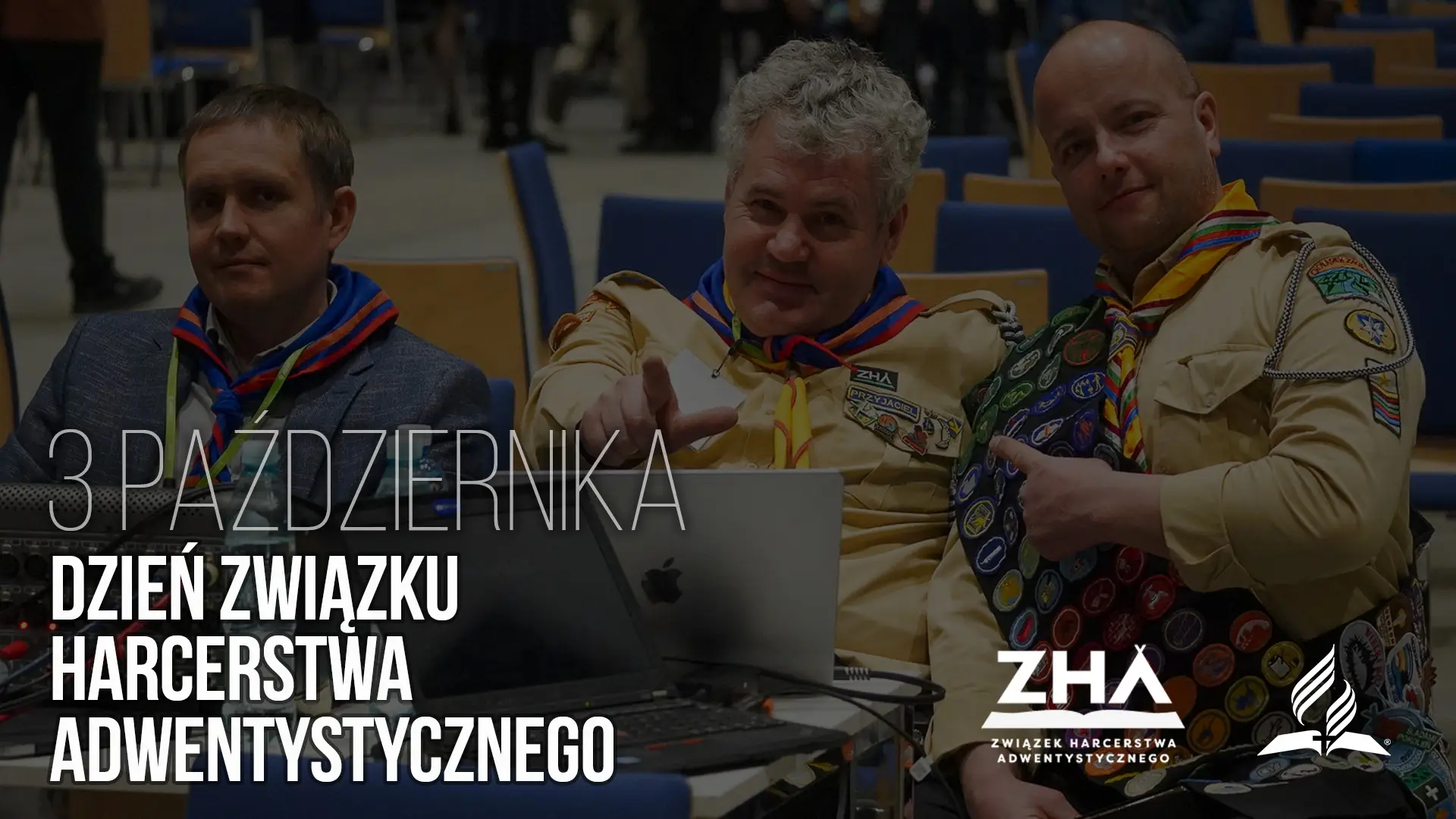 Троє чоловіків у скаутській формі з нашивками усміхаються перед камерою в залі