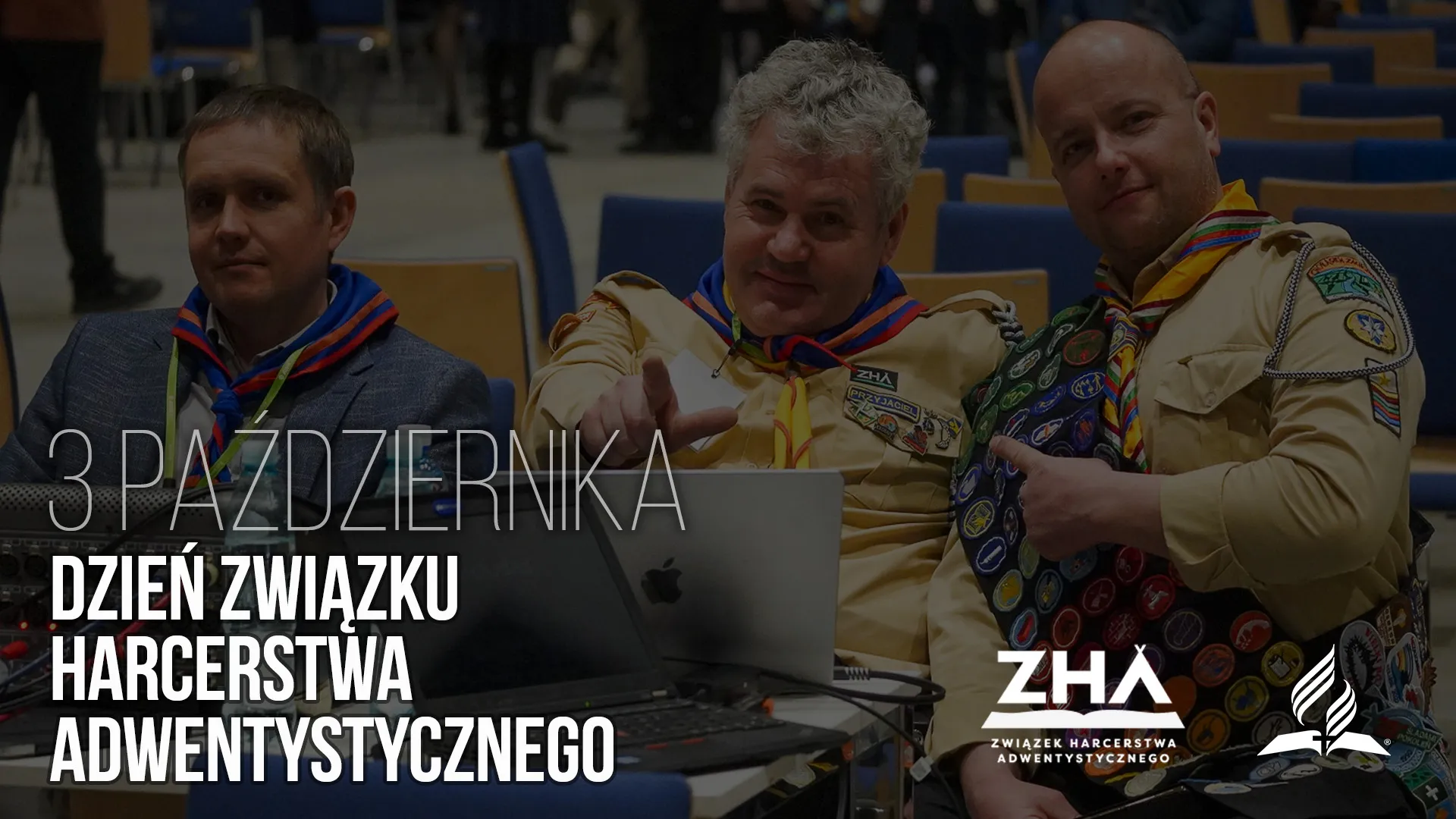 Троє чоловіків у скаутській формі з нашивками усміхаються перед камерою в залі