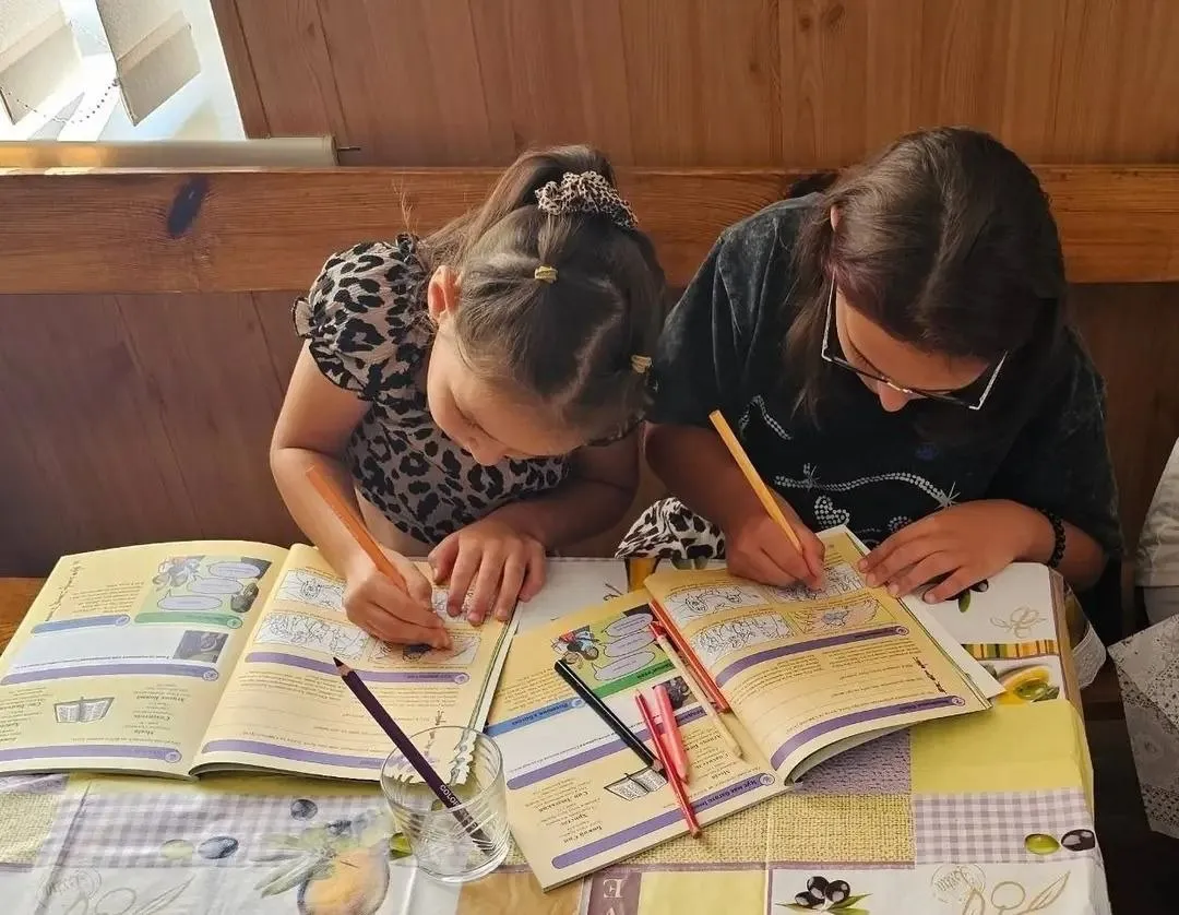 Дві дівчинки за столом олівцями розмальовують сторінки навчальних зошитів