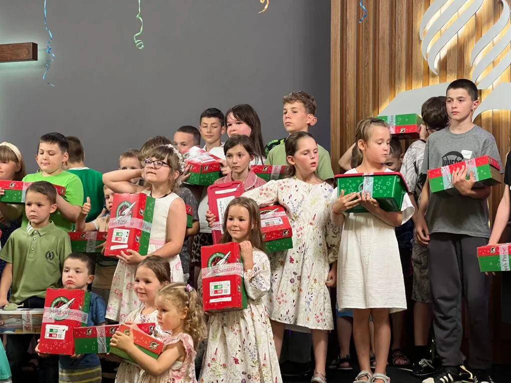 Велика група дітей стоїть із подарунковими коробками «Operation Christmas Child» у руках