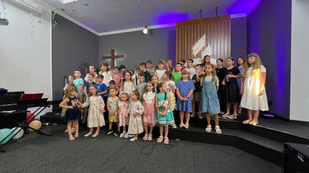 Велика група дітей у святковому одязі стоїть на сцені молитовного дому