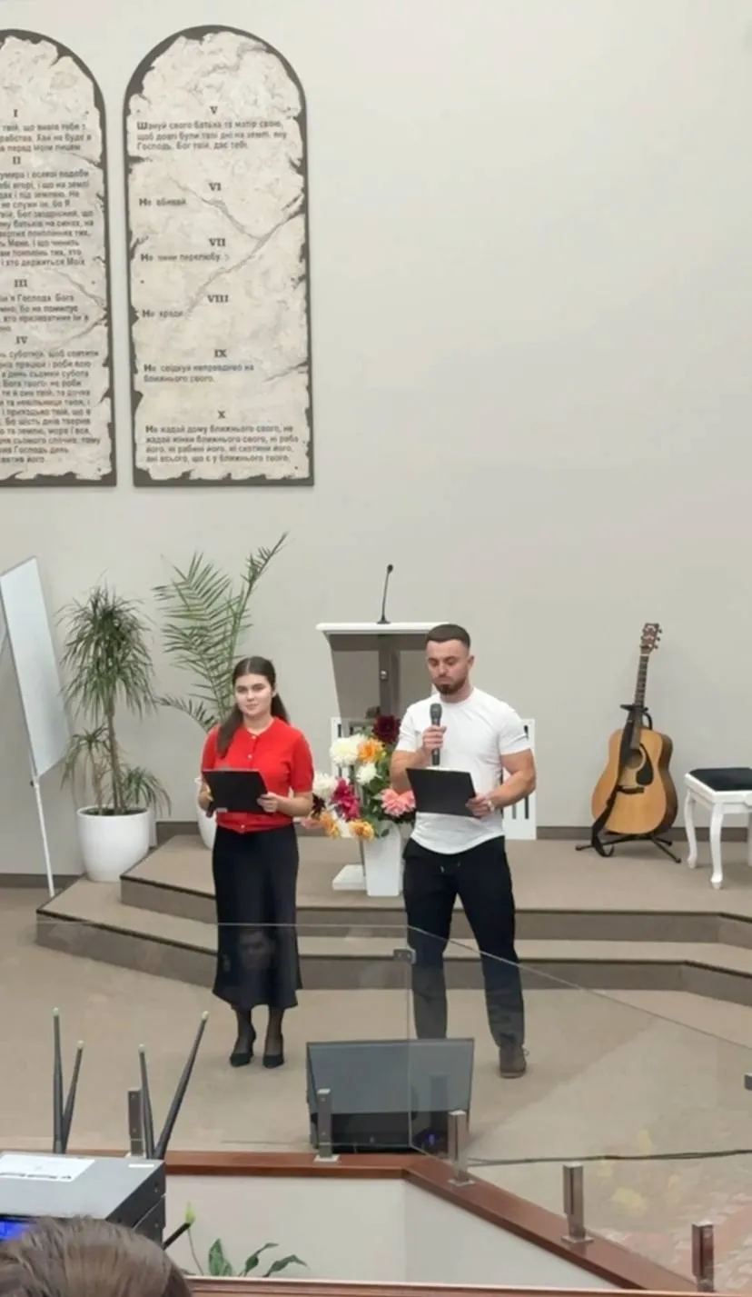 Дівчина та чоловік із мікрофоном ведуть програму на сцені церкви на тлі скрижалей з заповідями