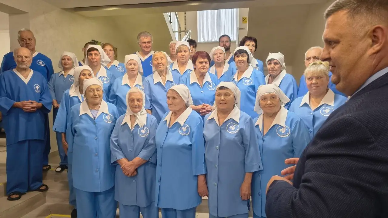 Група людей в однакових блакитних халатах з білими косинками слухає чоловіка в костюмі
