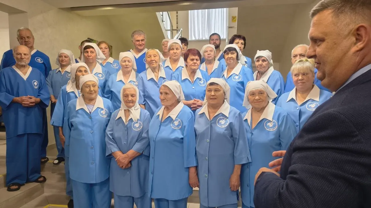 Група людей в однакових блакитних халатах з білими косинками слухає чоловіка в костюмі