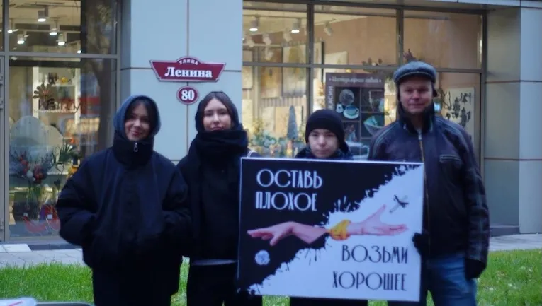 Четверо людей стоят на улице с плакатом «Оставь плохое — возьми хорошее»