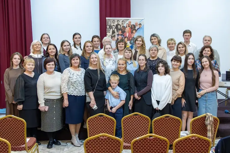 Большое групповое фото участниц и участников собрания в зале с красными креслами